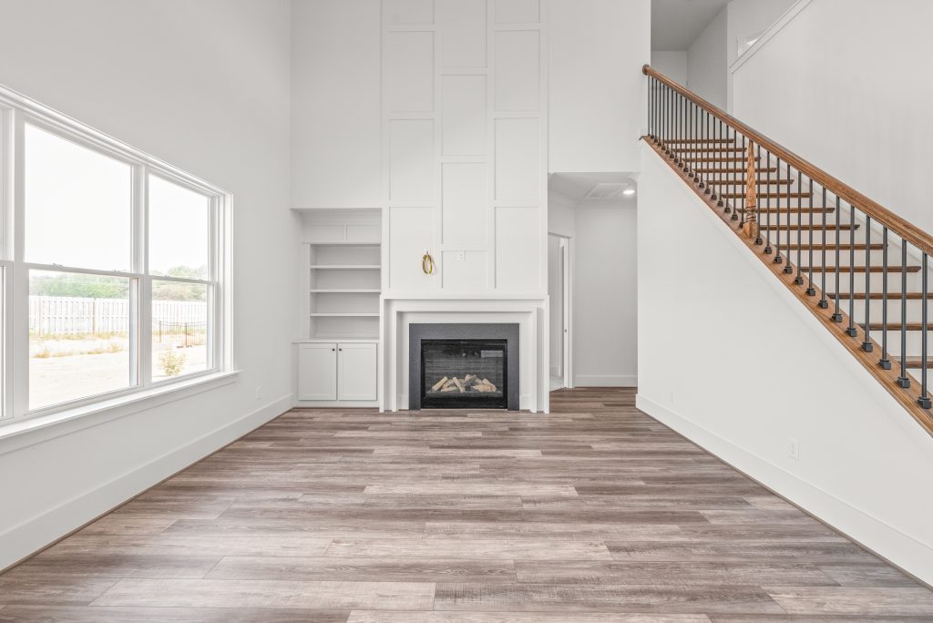 White fireplace in a living room with a large window and staircase with wooden railing